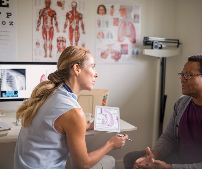 Female doctor with digital tablet talking with senior male patient in examination room