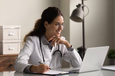 Smiling,Professional,Female,Doctor,Wearing,Glasses,And,Uniform,Taking,Notes