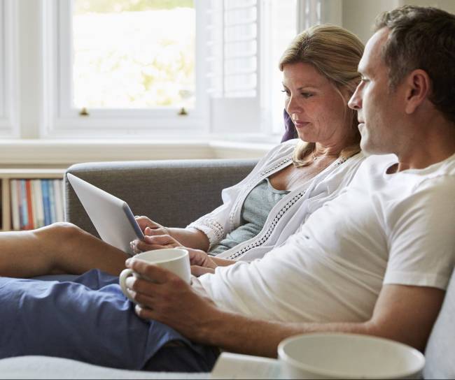 Un couple assis dans un sofa, regardant une tablette.