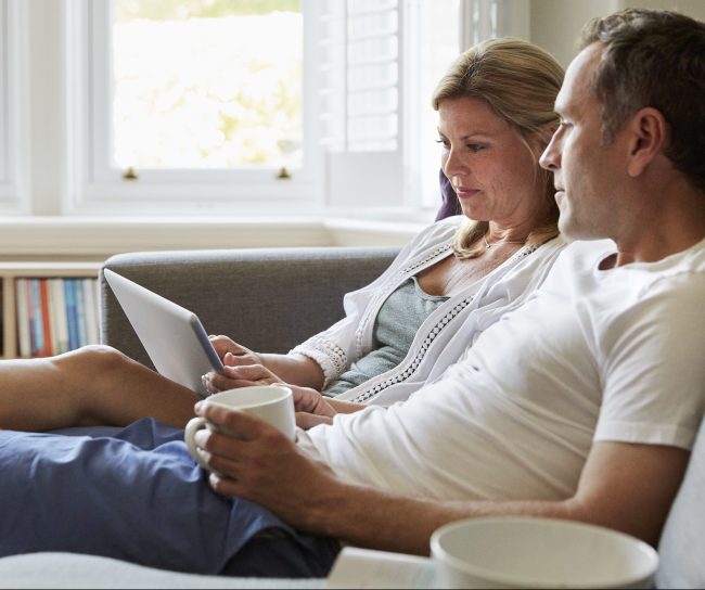 Un couple assis dans un sofa, regardant une tablette.