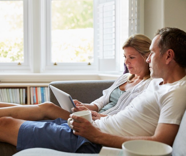 A couple seated on the sofa, a woman using a laptop computer, and a man looking into the distance.