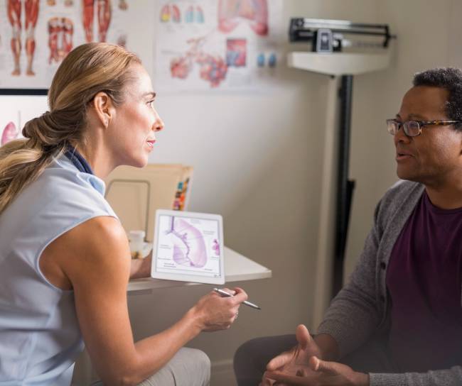 Female doctor with digital tablet talking with senior male patient in examination room
