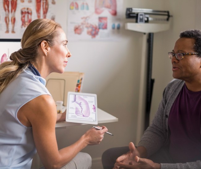Female doctor with digital tablet talking with senior male patient in examination room
