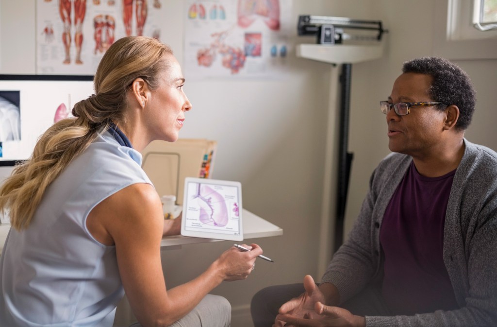 Female doctor with digital tablet talking with senior male patient in examination room